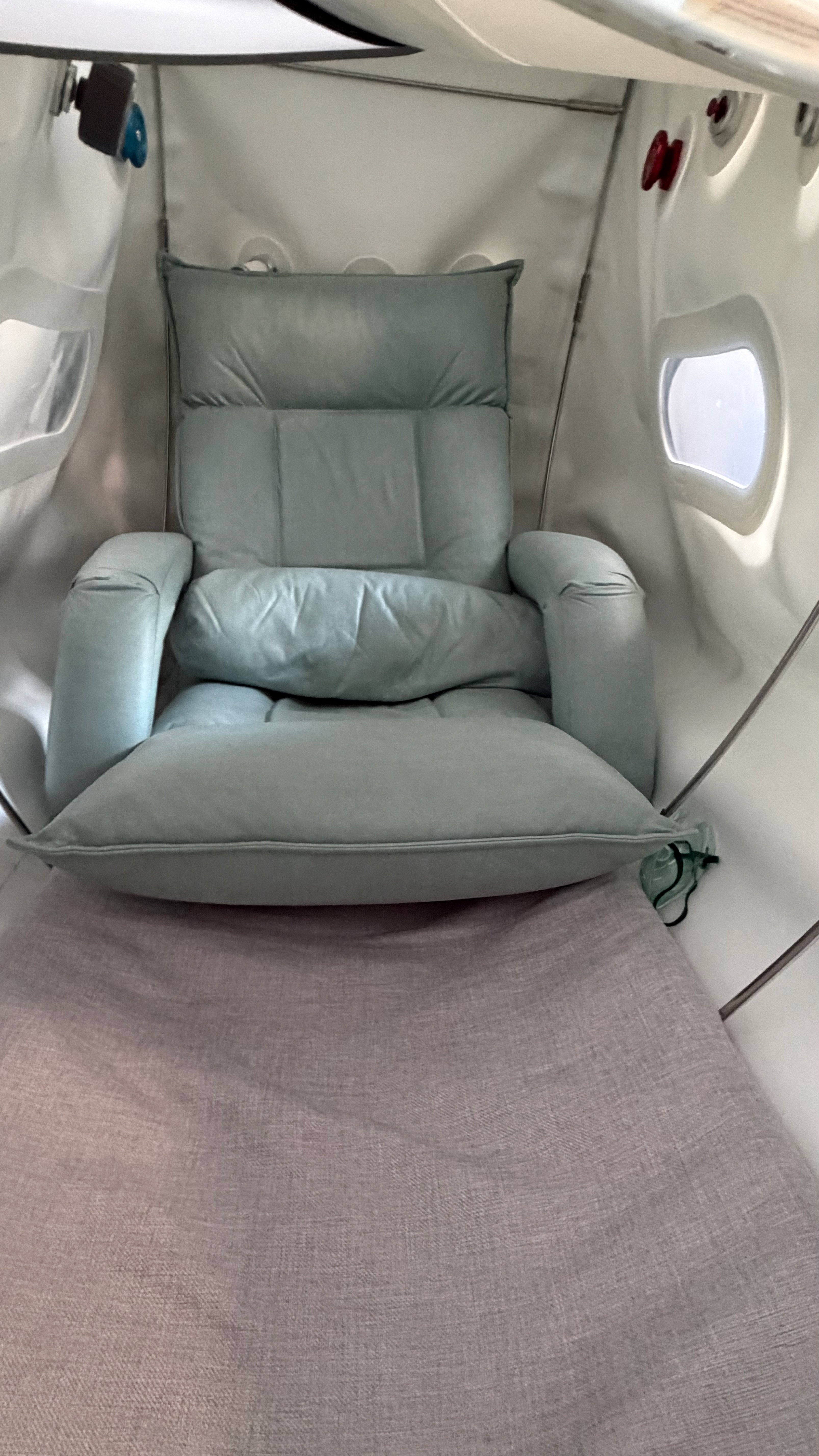 Used hyperbaric chamber Atlanta interior — inside the OXYREVO Forward90 Pro showing the adjustable sage-green folding chair (sit or recline), memory foam mattress, multi-layered viewing window and pressure relief valve. Actual photo of the included accessories with this used hyperbaric chamber for sale in Buckhead, Atlanta GA.